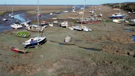 Various-stranded-abandoned-fishing-boat-wreck-shipyard-in-marsh-mud-low-tide-coastline-aerial-zoom-in-view
