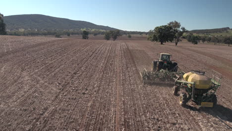 Aerial-view-of-drone-tracking-Tractor-towing-Air-Seeder-from-behind-in-a-large-paddock-with-big-hills-in-the-background-in-the-rural-town-of-Yerong-Creek,-Wagga-Wagga,-NSW-Australia