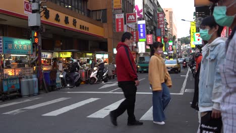 Taxi-Amarillo-Pasando-Por-Una-Calle-Concurrida-En-Keelung-Taiwán,-Y-Peatones-Con-Máscaras-Con-Conciencia-De-La-Pandemia-De-Covid-19