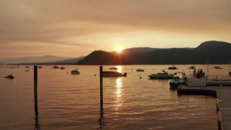 Niedrige-Luftaufnahme-Des-Kanadischen-Docks-Und-Sees-Mit-Booten-Und-Menschen-Während-Eines-Wunderschönen-Sonnenuntergangs-Am-Sommerabend