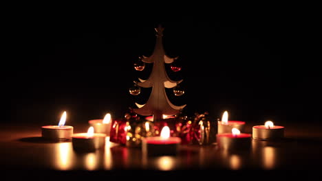 Isolated-Christmas-tree-figurine-adorn-trinket,-surrounded-by-candles-over-a-black-background