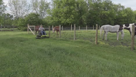 Man-Trimming-The-Grass-Using-An-Electric-Zero-Turn-Mower-Near-The-Pasture-Land-For-Horses