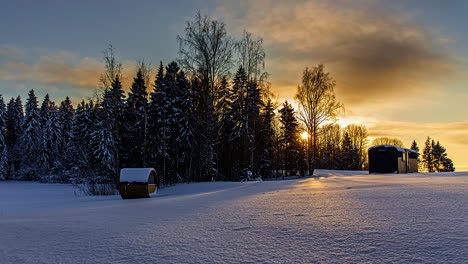 Sunset-in-winter-countryside-with-remote-cabin-and-barrel-sauna-outside,-timelapse