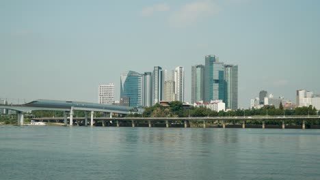 Centro-Comercial-Mecenatpolis,-Puente-Ferroviario-Dangsan-Sobre-El-Río-Han,-Tráfico-De-Automóviles-En-La-Vía-Rápida-Gangbyeon,-Frente-Al-Río-Hangang,-Torre-Seah-Y-Rascacielos-De-Seguros-Kb-Sobre-Fondo-De-Cielo-Azul,-Seúl