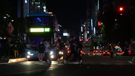 Commuter-Bus-Yields-As-Pedestrians-In-Masks-Cross-The-Street-In-Gangnam,-Seoul-At-Night-During-Covid-Pandemic-In-Korea