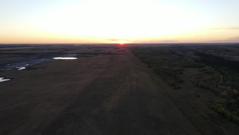 Drone-ascending-revealing-the-sun-setting-over-the-horizon-of-the-Alberta-countryside,-Canada