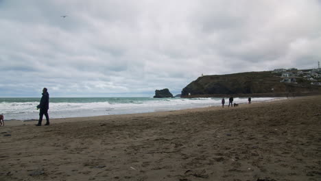 Menschen-Gehen-Im-Winter-Mit-Hunden-Am-Strand-Von-Portreath-Spazieren,-Während-Die-Wellen-An-Der-Küste-Von-Cornwall-Krachen