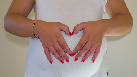 Woman-making-heart-symbol-on-her-belly-with-baby-inside,-static-view