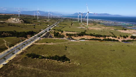 Green-electricity-windmill-farm-in-Vietnam-with-endless-highway,-aerial-drone-shot