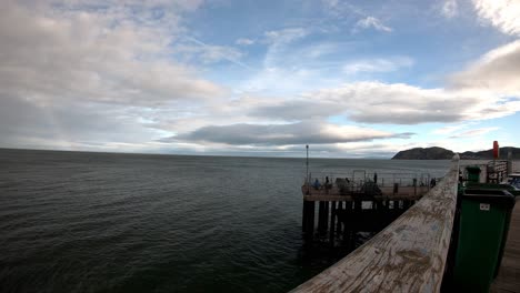 Zeitraffer-Von-Menschen,-Die-Vor-Dem-Hölzernen-Pier-Von-Llandudno-Angeln,-Mit-Blick-Auf-Den-Regenbogenbedeckten-Ozean