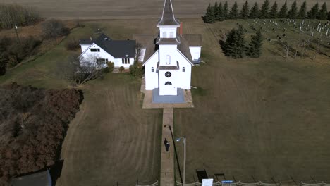 Lento-Movimiento-Aéreo-De-Retroceso-En-4k-Que-Revela-Una-Hermosa-Y-Antigua-Iglesia-Rural-Y-Una-Persona-Caminando-Hacia-Ella