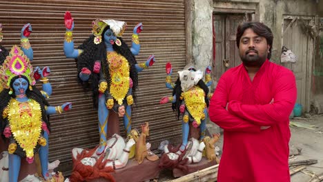Indian-man-in-red-kurta-standing-in-side-Goddess-kali-statues,-smiling-at-the-camera,-Diwali-festival
