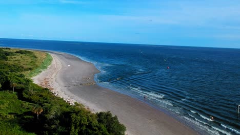 Blue-sky-and-ocean,-sandy-beach,-and-grassy-land-area-from-drone-view