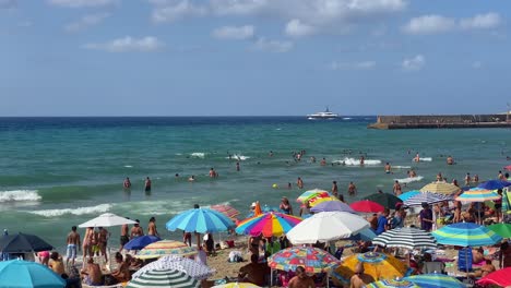 Yacht-Passiert-Im-Sommer-Einen-überfüllten-Strand-Mit-Sonnenschirmen-Am-Mittelmeer