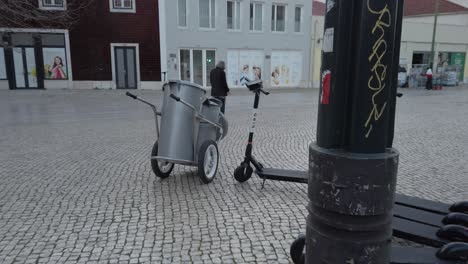 Moderno-Scooter-Eléctrico-Estacionado-Con-Carrito-De-Basura-En-La-Antigua-Calle-Adoquinada-De-Lisabon,-Portugal