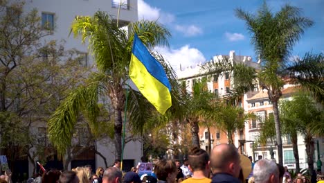 Ukrainian-flag-being-waved-high-above-crowds-during-protests-in-Malaga,-Spain