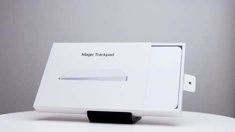 Caja-De-Paquete-Blanca-Giratoria-Medio-Abierta-Que-Muestra-El-Trackpad-Mac-Magic-En-El-Soporte-De-Exhibición-Con-El-Logotipo-De-La-Empresa-Apple-Visible-En-El-Lateral