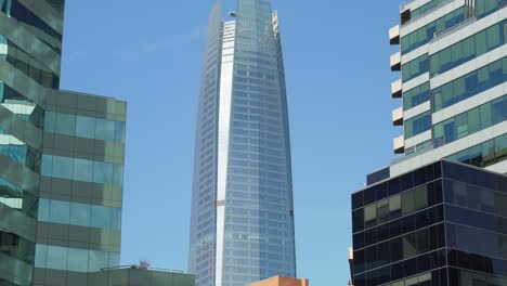 Tilt-down-of-Costanera-Center-skyscraper-surrounded-by-modern-buildings-at-daytime,-Santiago,-Chile