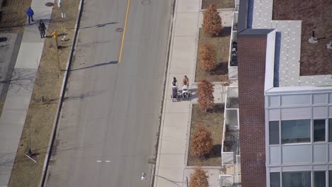 People-walking-children-babies-in-stroller-near-park-in-city---Two-females-couple-walking-with-strollers-in-city-top-down-aerial-view-from-balcony---LGBTQ+-or-two-mother-friends-walking-together-baby