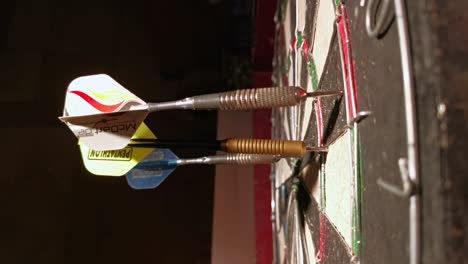 Several-darts-hitting-an-old-dart-board-in-front-of-a-dark-background