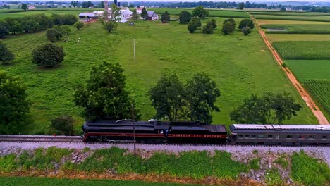 Una-Vista-Aérea-Paralela-De-Un-Antiguo-Tren-De-Pasajeros-De-Vapor-Que-Sopla-Humo-Negro-A-Través-De-Las-Tierras-Agrícolas-De-Pensilvania