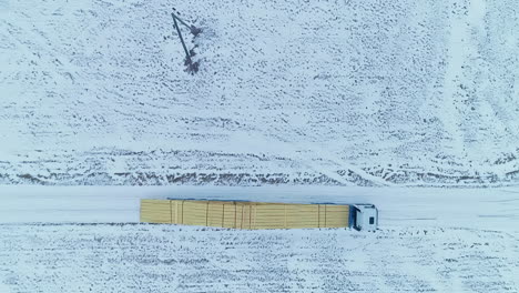 Aerial-top-down-shot-of-Truck-transporting-Wood-Logs-for-Roof-Building-on-snowy-road-in-winter