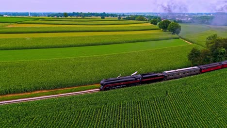 Una-Vista-Aérea-Paralela-De-Un-Antiguo-Tren-De-Pasajeros-De-Vapor-Que-Sopla-Humo-Negro-A-Través-De-Las-Tierras-Agrícolas-De-Pensilvania