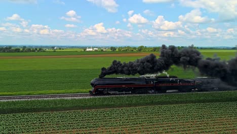 Eine-Parallele-Luftaufnahme-Eines-Antiken-Dampfzugs,-Der-An-Einem-Sonnigen-Tag-Mit-Schwarzem-Rauch-Durch-Ackerland-Fährt