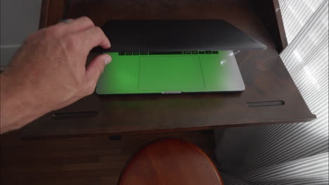 Hand-closes-laptop-computer-with-green-screen-for-chroma-key