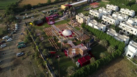 rotational-footage-of-an-event-space-surrounded-by-cars-and-buildings,-outdoor-bright-day-view,-multiple-symmetrical-chair-set-up,-green-grass-and-lawn-foundation,-big-white-dome-in-center,-gold-vibe