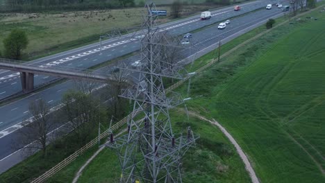 Speeding-traffic-passing-pylon-electricity-tower-on-M62-motorway-aerial-view-reversing-shot