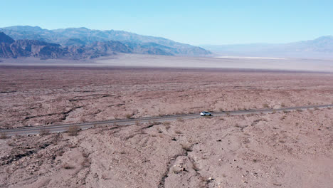 Cinematic-aerial-shot-of-white-Tesla-car-moving-in-the-middle-of-Mojave-Desert