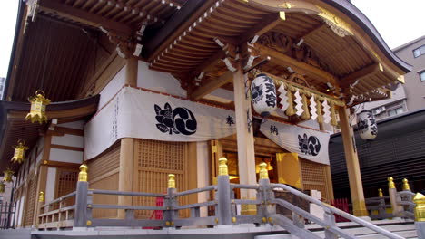 TOKYO,-JAPAN-circa-April-2020:-woman-worshipping-at-traditional-Japanese-shrine,-gorgeous-art-craft-roof-with-paper-lanterns,-in-peaceful-approach,-on-spring-evening,-day,-TILT-DOWN