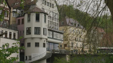 Toma-Panorámica-Desde-La-Vista-Lejana-De-La-Torre-De-La-Escalera-Medieval-Hasta-Una-Vista-Más-Cercana-De-Una-Mujer-Elegante-Hablando-Por-Teléfono-Mientras-Está-Sentada-En-Un-Banco-En-El-Río-Del-Centro-De-Tubingen-En-Balvaria,-Alemania,-Europa