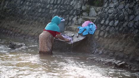 Das-Wirkliche-Leben-Einer-Alten-Frau-In-Vintage-Dorfkleidung,-Die-Am-Fluss-Steht-Und-Wäsche-Wäscht