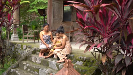 two-daughters-and-a-mother-accompanying-her-child-to-play-Dakon,-a-traditional-Javanese-game-on-the-terrace-of-the-house
