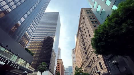 Looking-up-at-the-Los-Angeles-city-skyline-while-driving-along-a-downtown-street---bird-flying