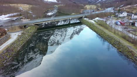 Bridge-with-road-E16-crossing-Gudvangen-river-Norway---Forward-moving-aerial-above-naeroy-valley-river-with-beautifu-mountain-reflections-in-water-surface