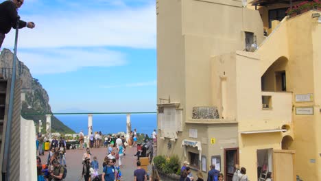 Tilting-down-medieval-European-style-architecture-in-with-chruch,-mountains-and-tourists-sightseeing-in-Capri,-Italy