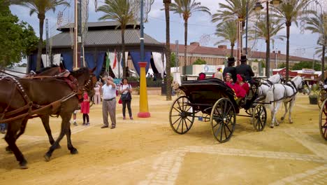 Horses-pull-carriages-of-Spanish-people-in-traditional-flamenco-outfits-at-Fair