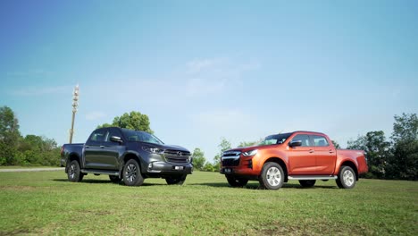 Malaysia,-March-13,-2022:-two-4x4-Isuzu-D-Max-pick-ups-in-dark-orange-color-and-black-on-a-grassy-field