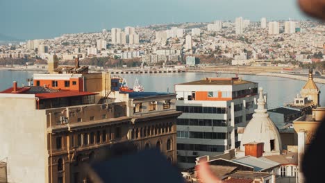 Fokusständer-Eines-Jungen-Mannes,-Der-Eine-Drohne-Mit-Fernbedienung-Steuert-Und-Im-Hintergrund-Die-Stadt-Valparaiso,-Chile,-Enthüllt