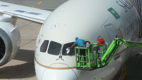 Un-Trabajador-Limpia-La-Ventana-Delantera-De-Una-Aerolínea-De-Bandera,-Arabia-Saudita,-Aerolínea-Saudita,-El-Avión-Se-Ve-En-La-Pista-Del-Aeropuerto-Internacional-De-Jeddah