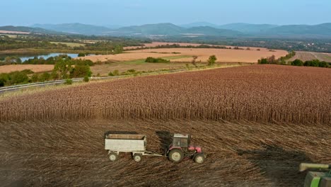 Sobrevuelo-Aéreo-De-Cosecha-De-Maquinaria-Agrícola-En-Campos-De-Girasoles-Búlgaros-Con-Colinas-De-Elena-Balcanes-En-Segundo-Plano