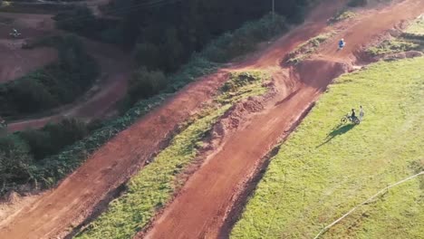 Drohnenaufnahme-Von-Motocross-Fahrern,-Die-Motorräder-Auf-Einer-Unbefestigten-Parkstrecke-über-Die-Linke-Kurve-Fahren-Und-Schnell-Springen