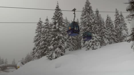Following-a-gondola-lift-moving-downwards-during-heavy-snowfall,-medium-shot