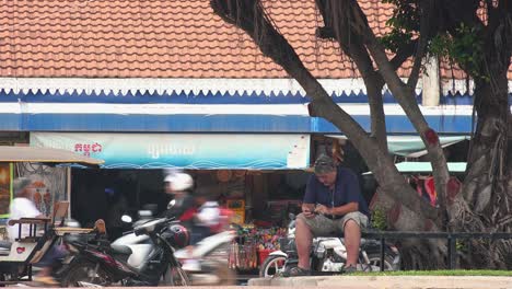 Hombre-En-Un-Banco-Usando-Su-Teléfono-Junto-Al-Antiguo-Mercado