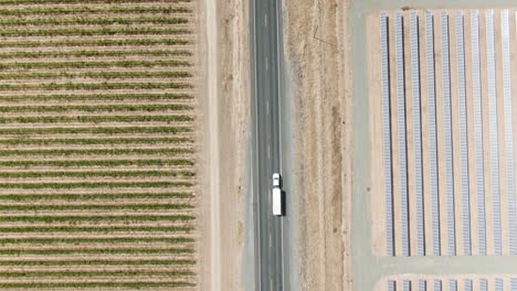 High-altitude-birdseye-view-over-a-local-country-road-surrounded-by-solar-panels-on-the-right-hand-side-and-a-vineyard-on-the-left-hand-side