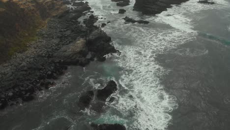 Aerial-drone-shot-flying-along-the-coast-while-waves-crash-against-the-rocks-in-a-cloudy-day-4K
