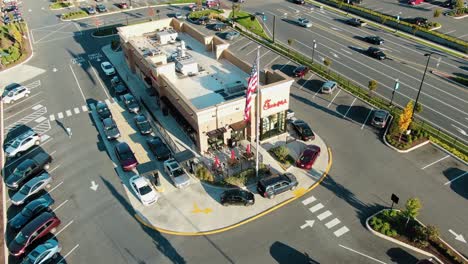 La-Inclinación-Aérea-Hacia-Arriba-Revela-Un-Camino-Muy-Transitado-De-Dos-Carriles-De-Chick-fil-a,-Bandera-Estadounidense